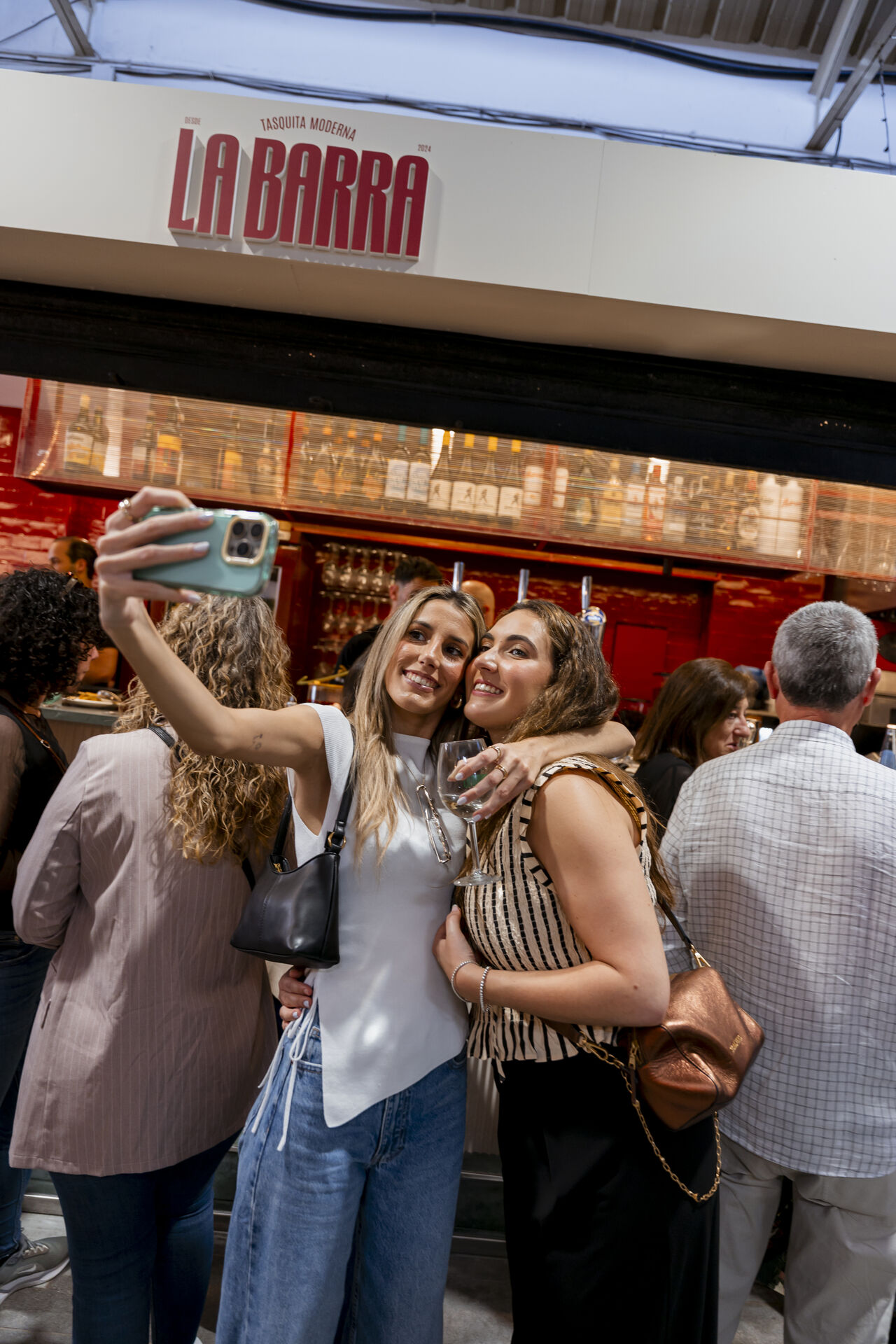 Clientes brindando en la barra de La Barra de Bendita bajo el rótulo luminoso